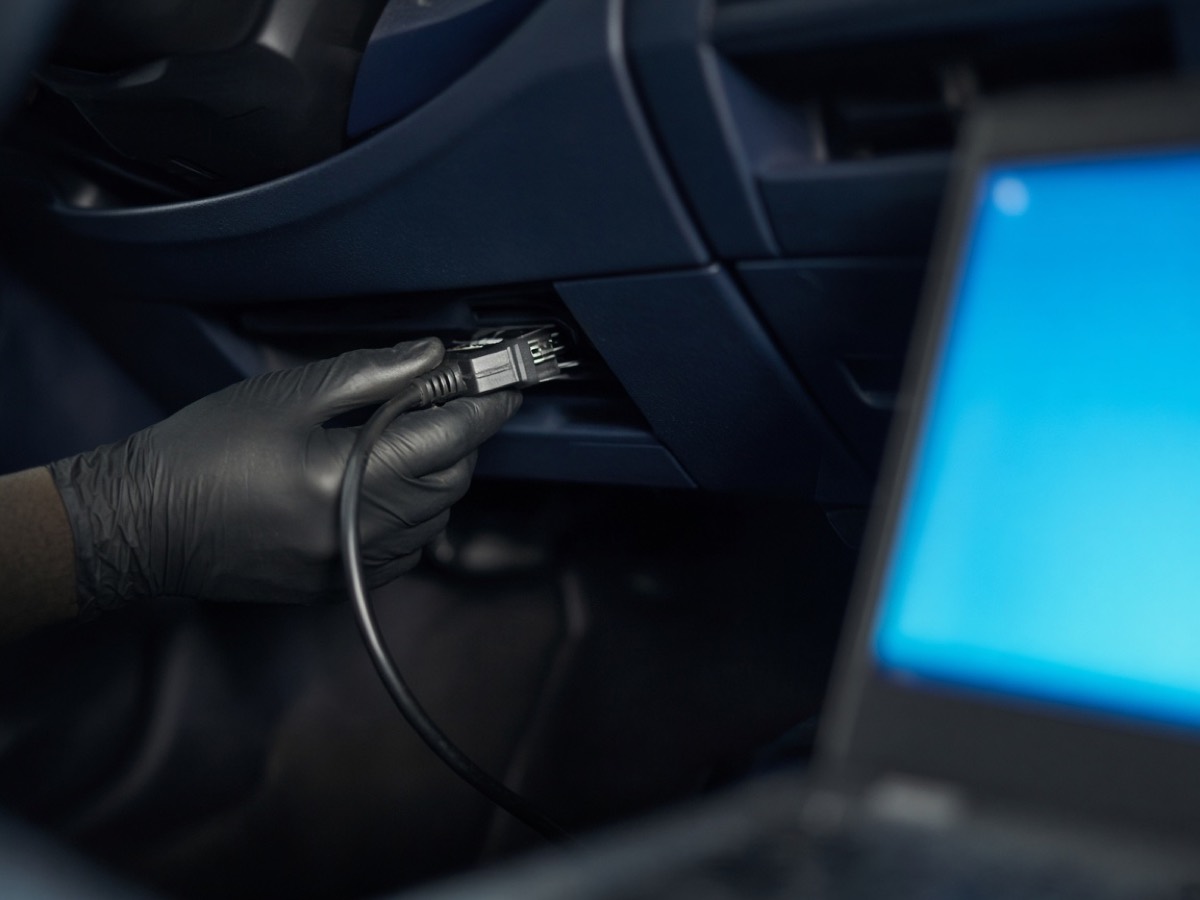 Diagnostic cable plugged in under a dashboard, screen unreadably blurred